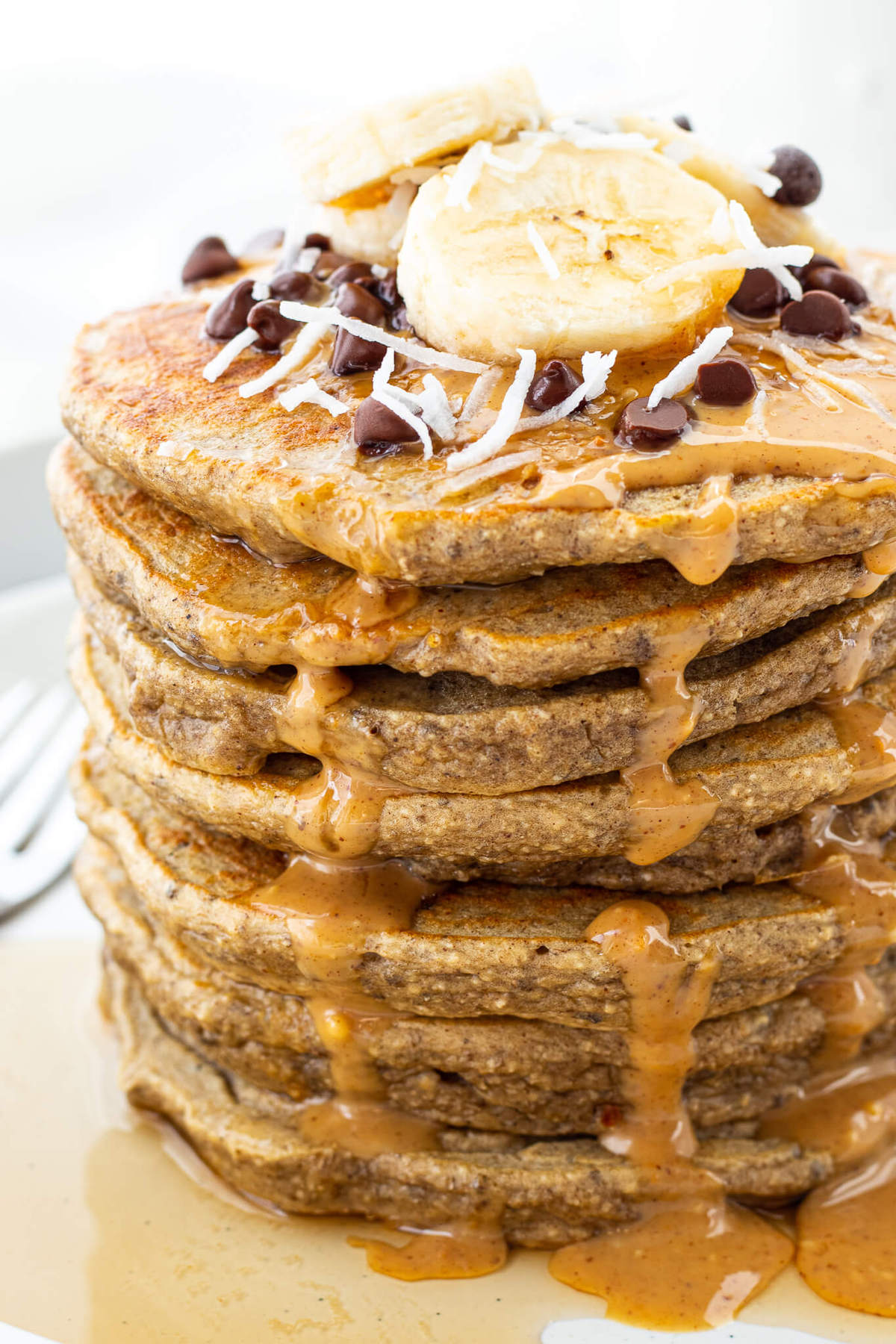 Up close image of a stack of banana protein pancakes with banana, peanut butter and chocolate chips.