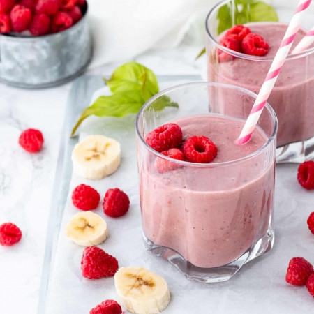 raspberry protein shake in glasses with fresh bananas and raspberries