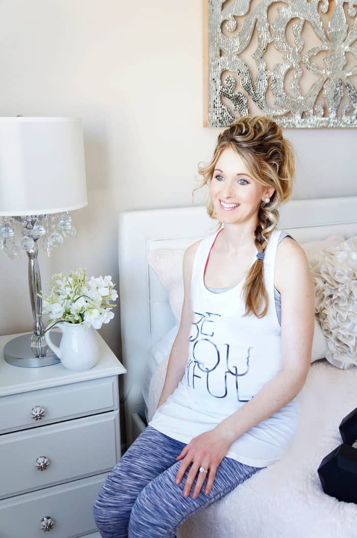 Elysia in a white tank sitting on the side of a bed