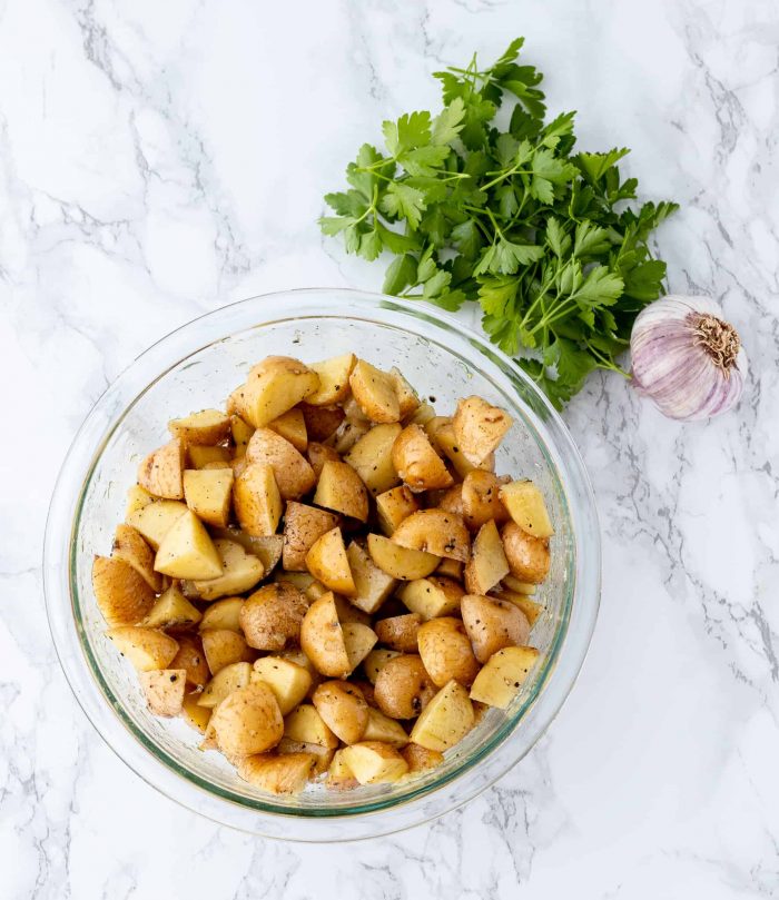 Diced potatoes in a bowl next to parsley and garlic.