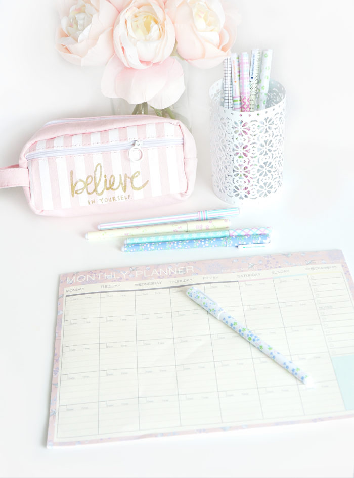 Monthly planner with colorful, pastel pens, a bag that reads \"believe in yourself\" and a pink flower