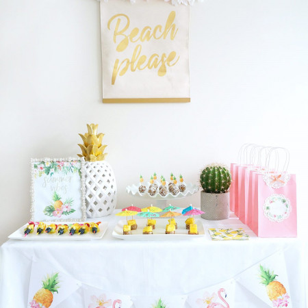 Table set with colorful food and decorations under a banner that says "Beach please"