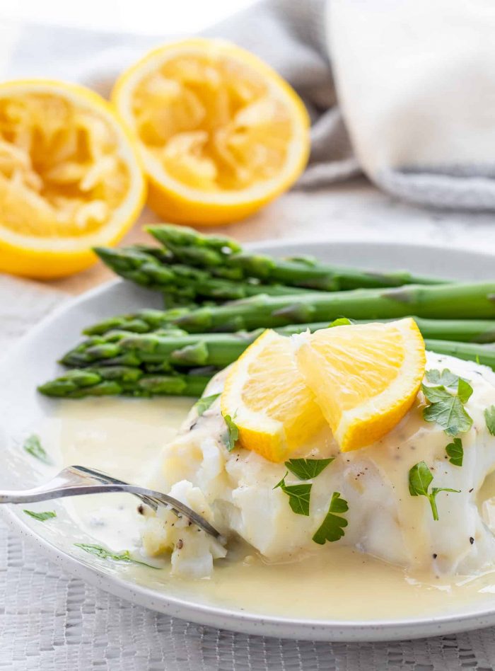 Using fork to eat fish with lemon sauce and asparagus