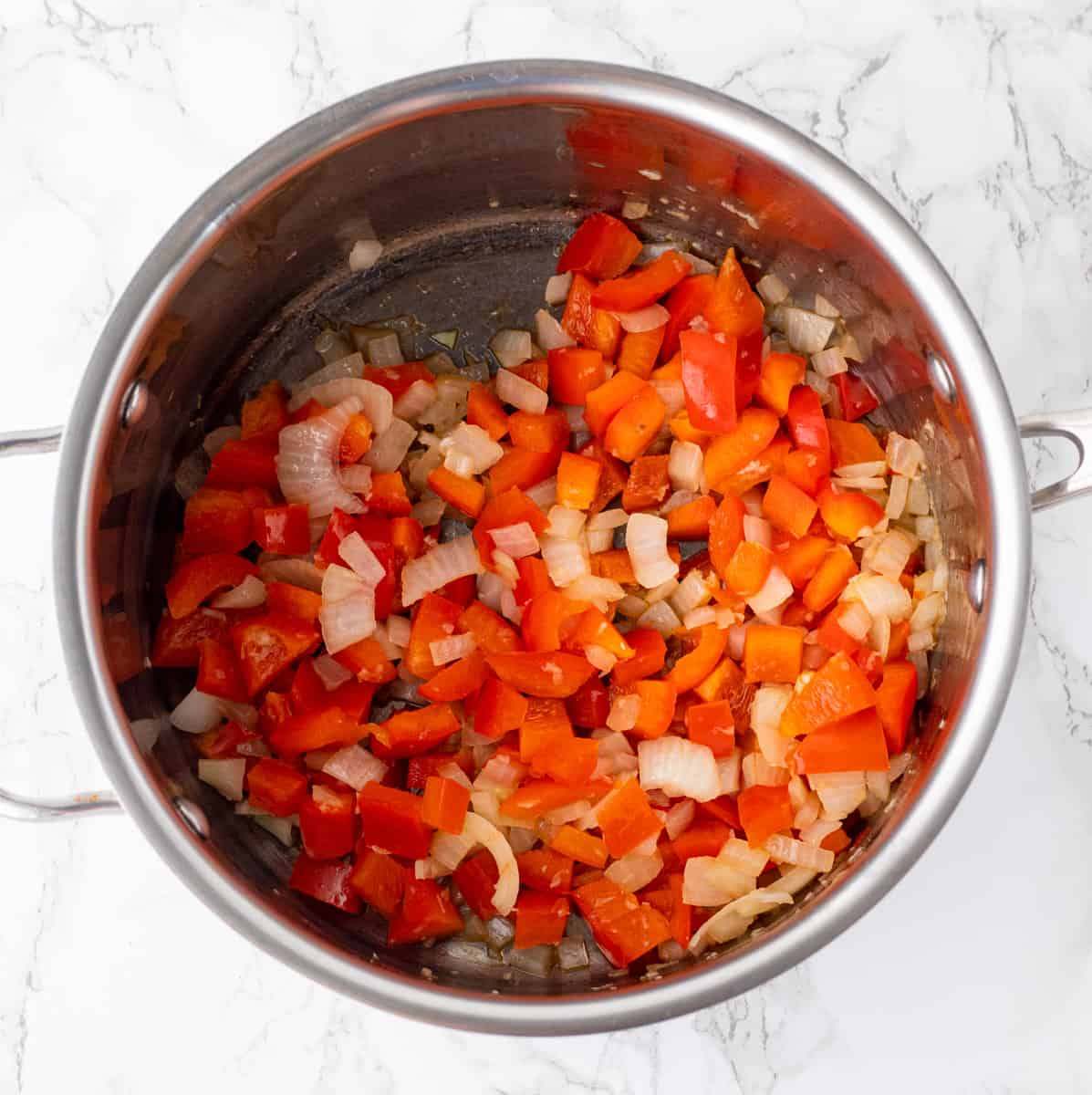 red peppers and onions cooking in a large sauce pan on marble background