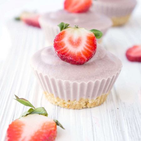 Line of No-Bake Vegan Strawberry Cream Cheesecake Cups with sliced strawberries on the side