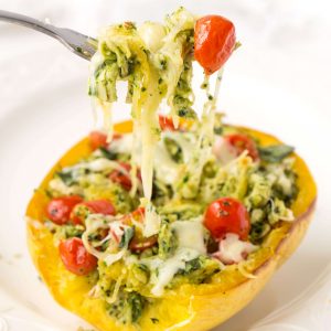 A fork with pesto chicken, melted cheese, spaghetti squash and diced tomatoes on a white plate