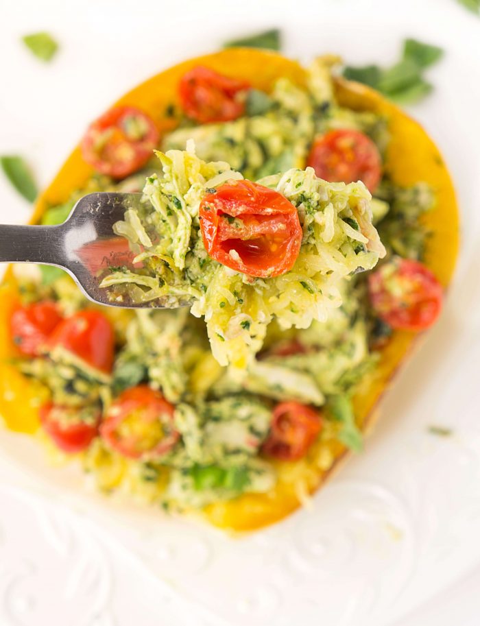 A close up of a fork with pesto chicken, melted cheese, spaghetti squash and diced tomatoes