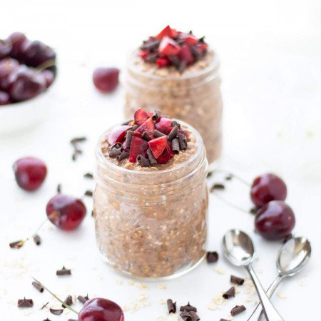 Two jars of Chocolate Cherry Overnight Oats surrounded by cherries and chocolate shavings