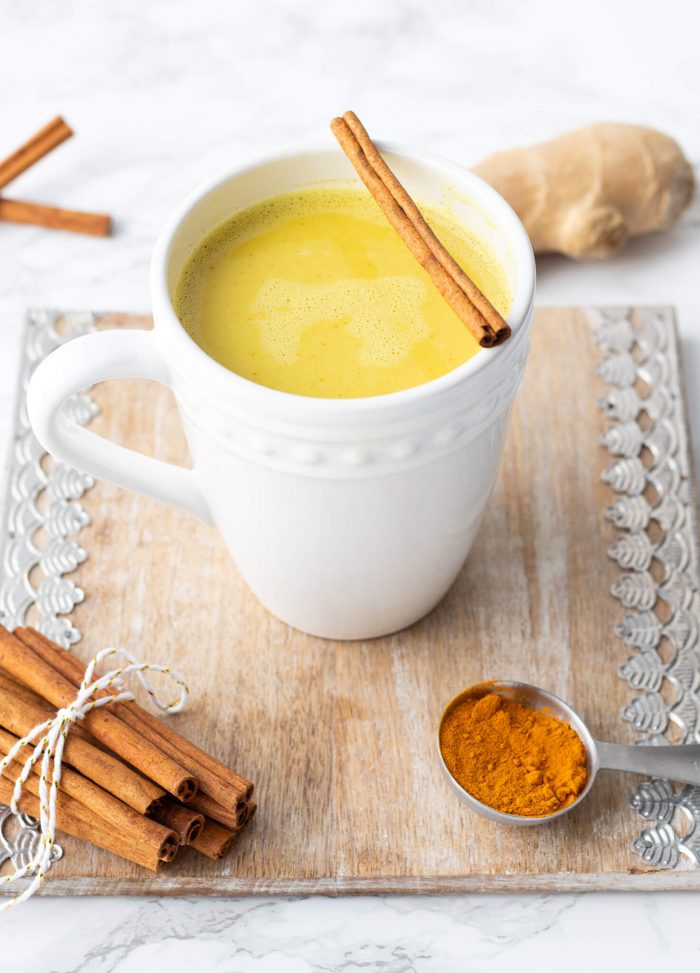 Turmeric latte with spoonful of turmeric, cinnamon stick and ginger.