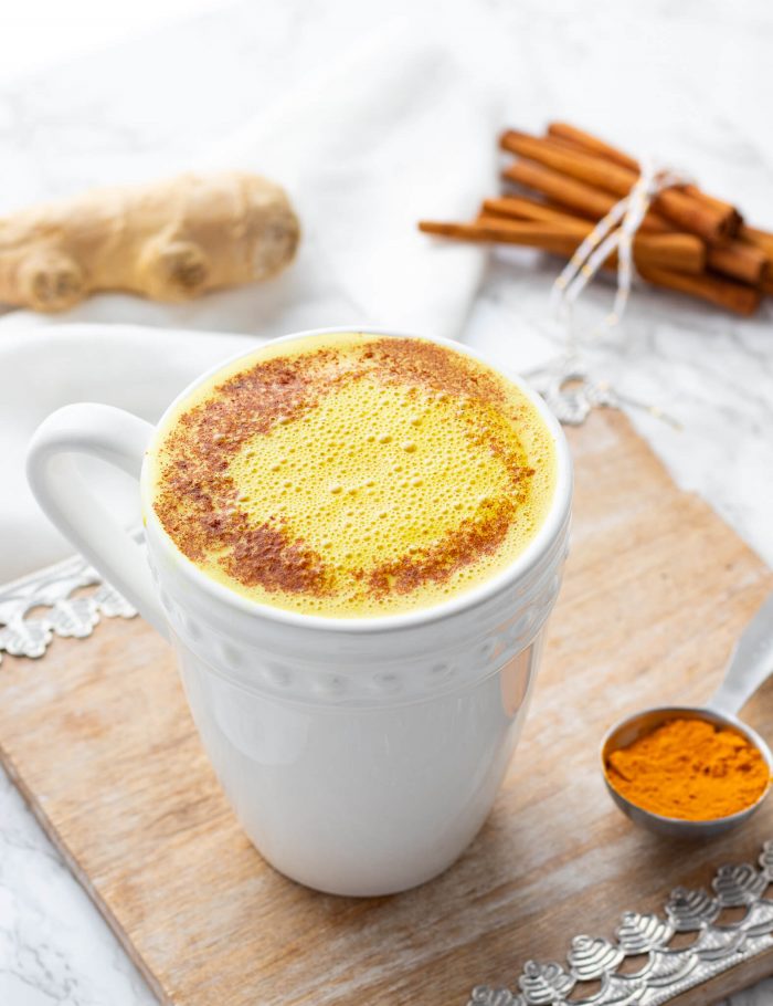 turmeric latte with spoonful of turmeric, cinnamon stick and ginger