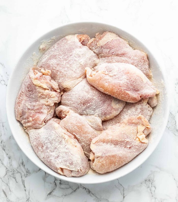 Chicken thighs coated in flour in a white bowl