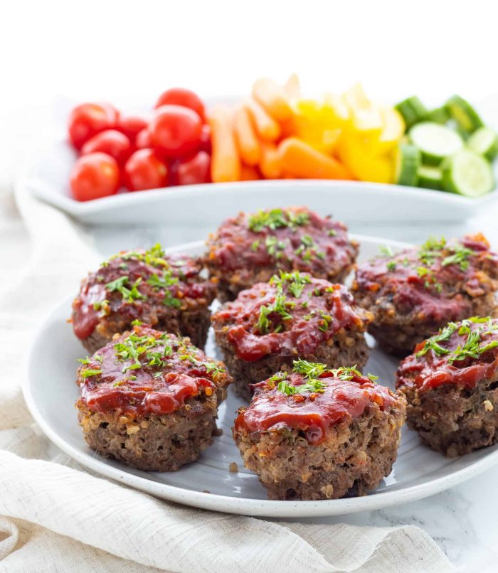 Mini meatloves on a plate topped with sauce and garnished with herbs