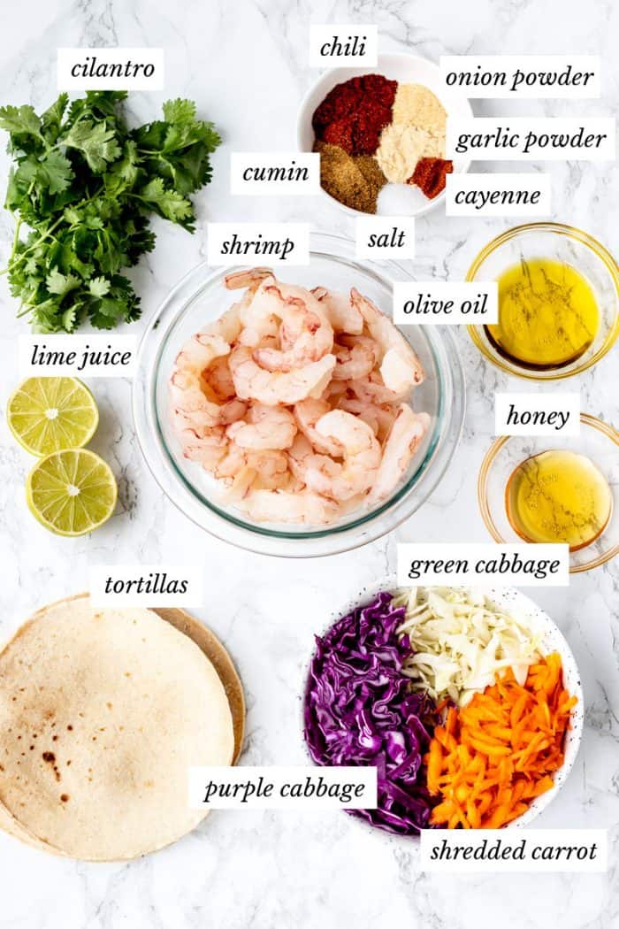 ingredients for the shrimp tacos on a marble background with labels