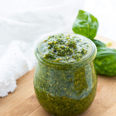 Dairy-free pesto in a small glass jar next to fresh basil leaves.