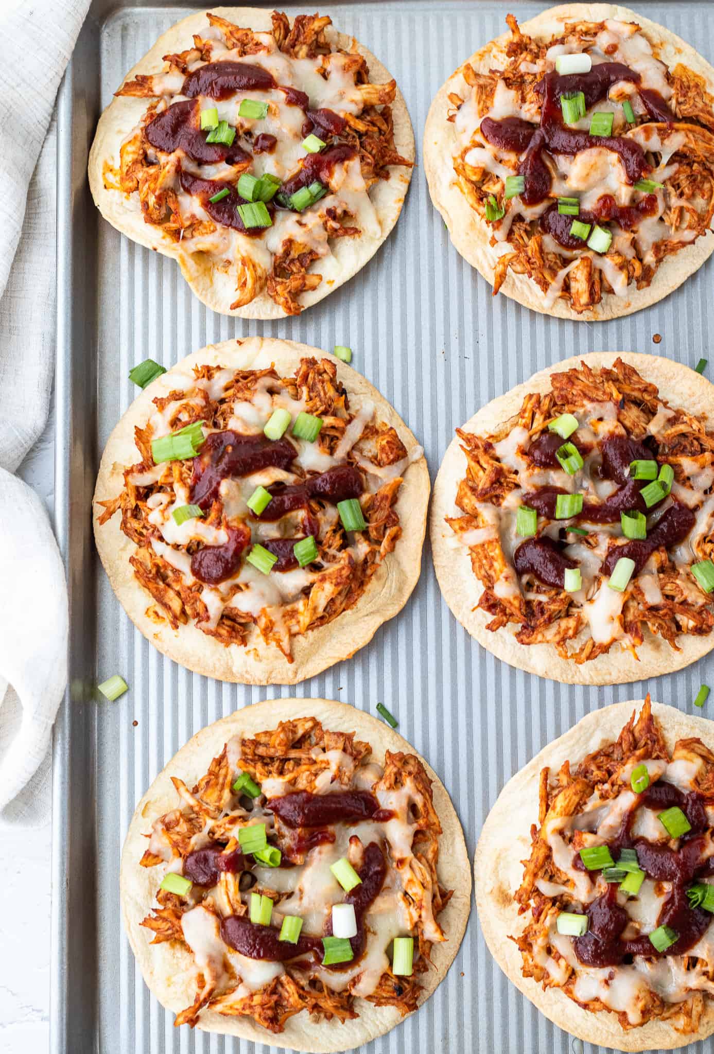 baked chicken tostadas topped with BBQ sauce and diced green onion on a baking sheet