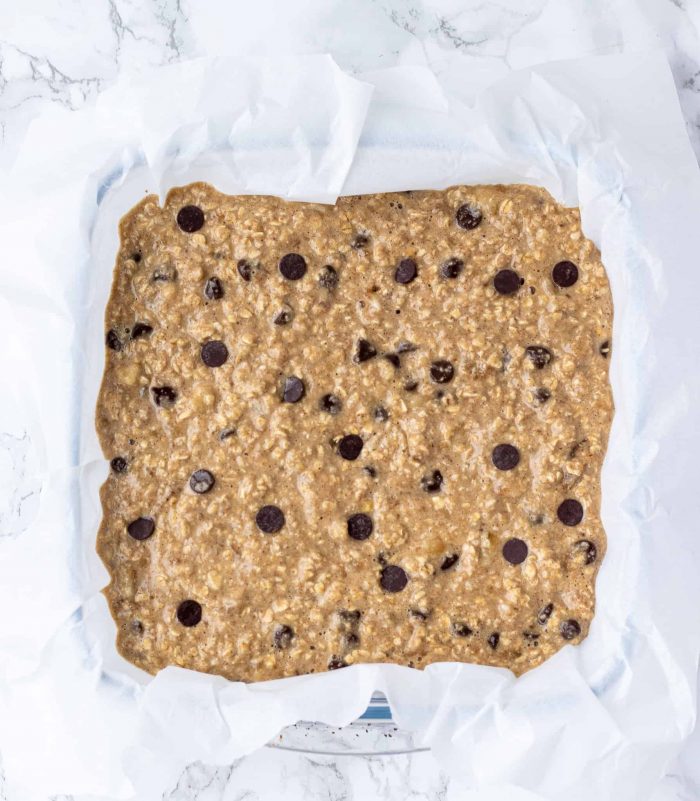 The oatmeal breakfast bars mixture poured into the baking dish lined with parchment paper.