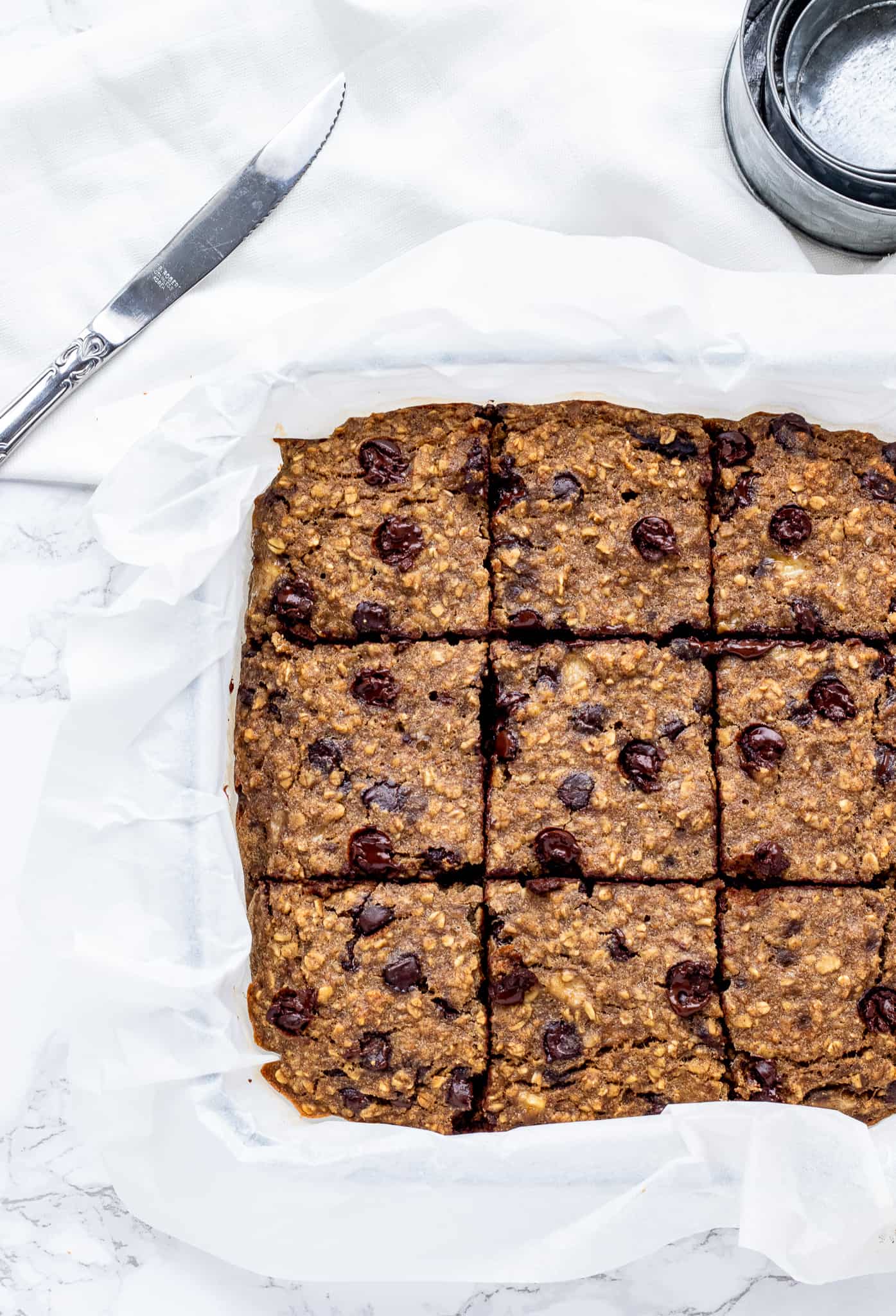 The baked oatmeal mixture cut into bars in a pan on parchment paper.