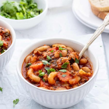 A spoon in a bowl of soup with beans, sausage and spinach