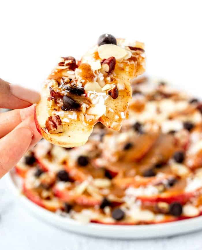 holding a couple of apple nachos with caramel drizzle and toppings