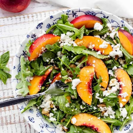 arugula nectarine salad topped with feta and chopped walnuts in a blue and white bowl with a fork