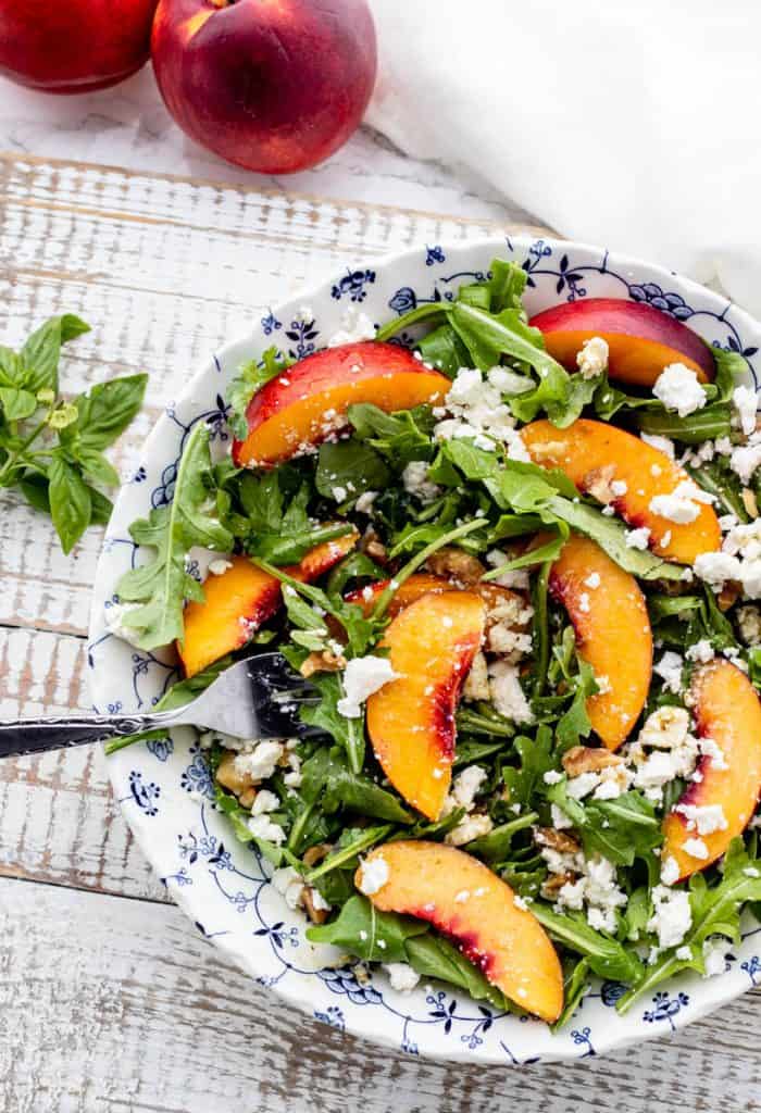 arugula nectarine salad topped with feta and chopped walnuts in a blue and white bowl with a fork