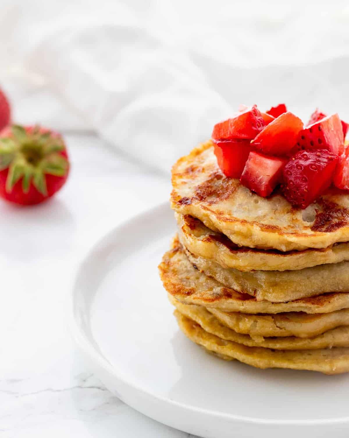 stack of pancakes topped with diced strawberries with napkin and fresh strawberries in background
