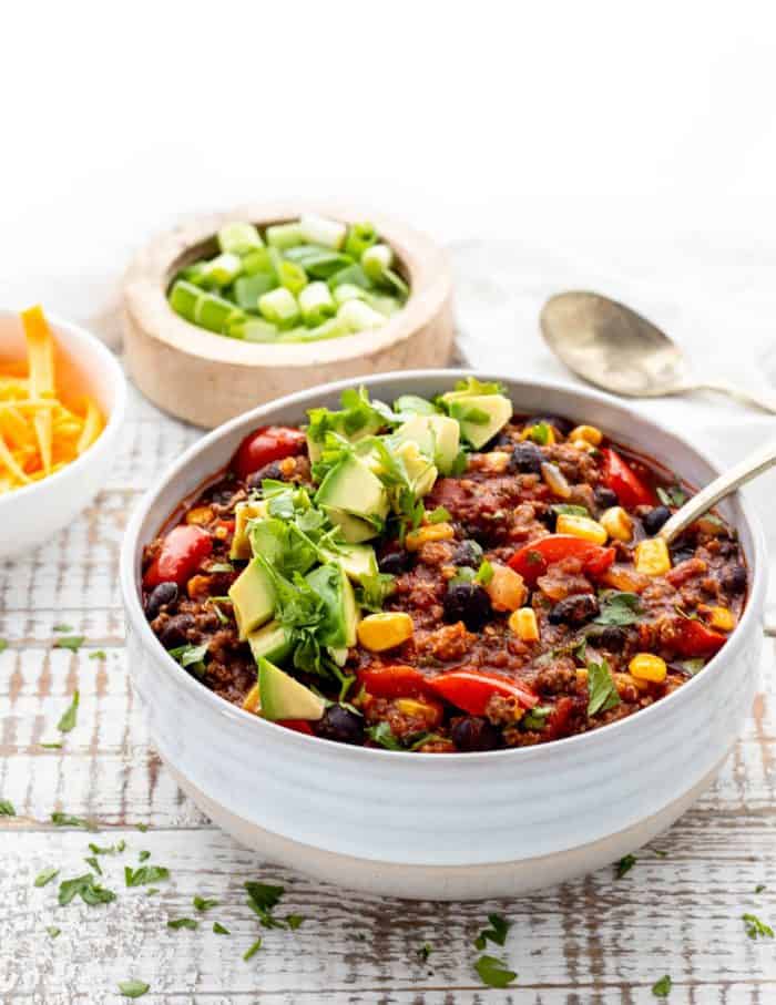 bowl of beef and quinoa chili with a spoon and diced avocado and cilantro