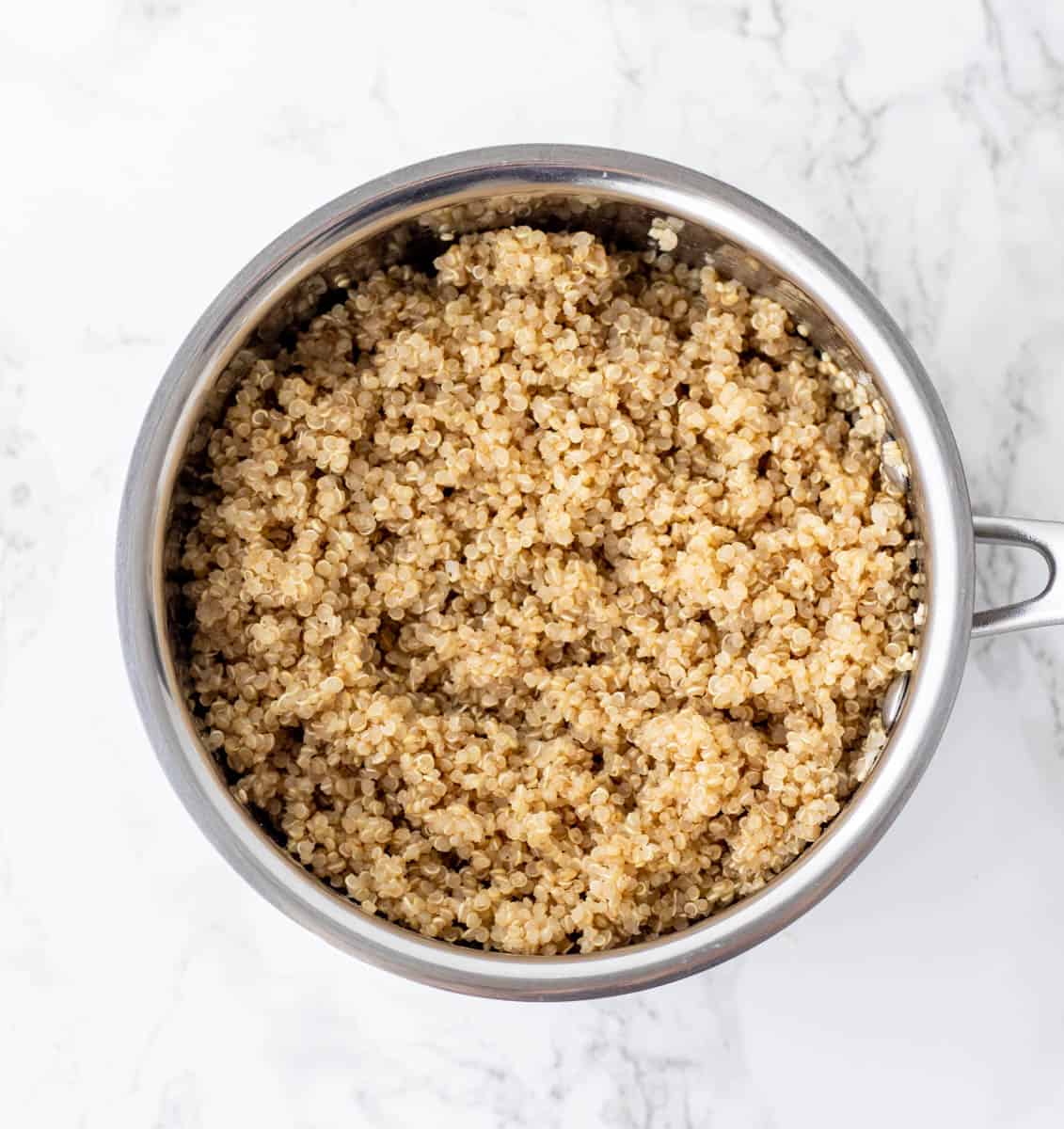 Cooked pot of quinoa on marble background.