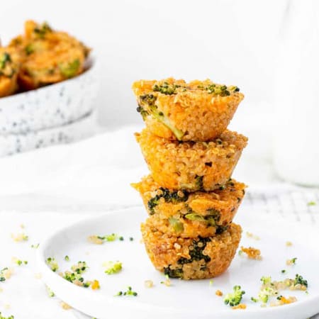 Stack of broccoli cheddar quinoa bites on white plate with speckled bowl of quinoa cups in background.