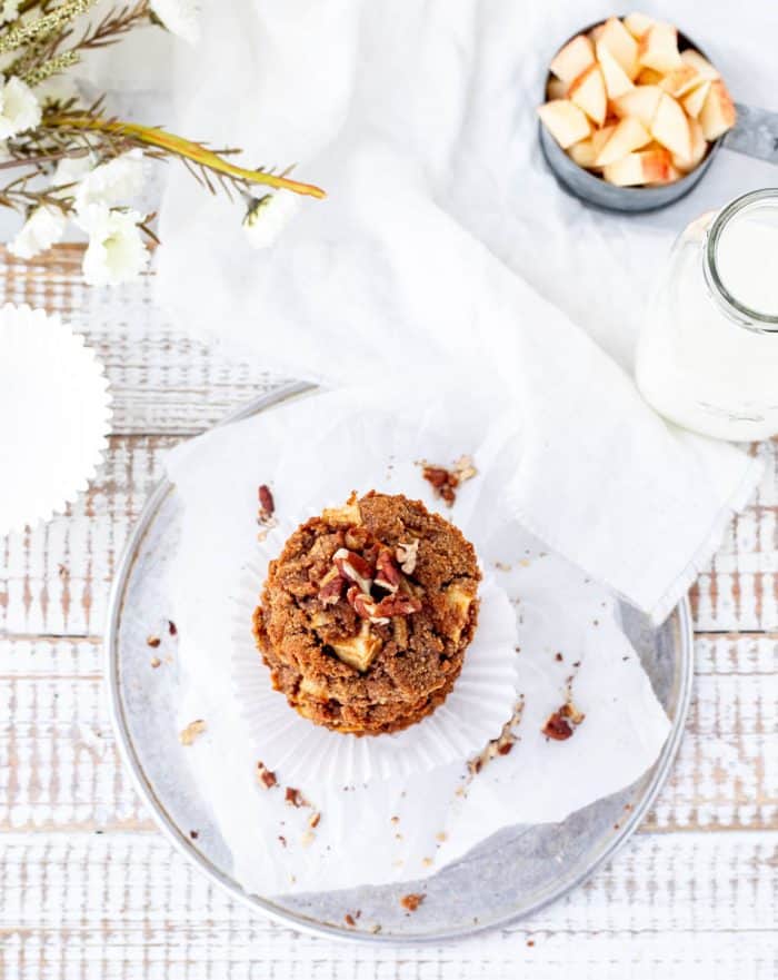 top shot of an apple muffin on a rustic wooden white background with chopped apples, milk and flowers