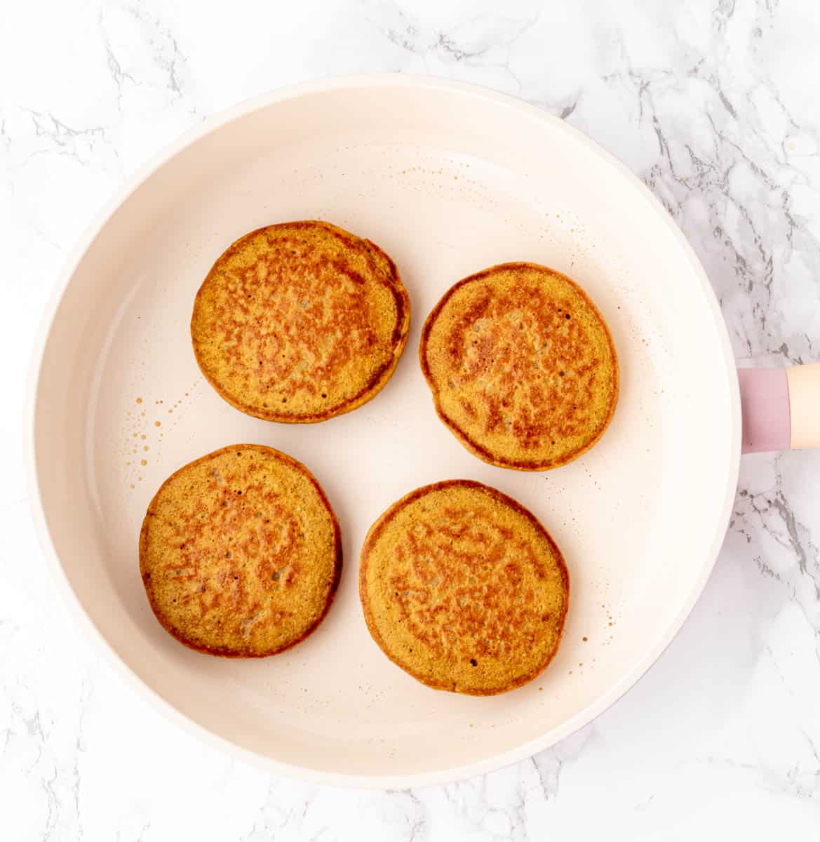 Cooked pumpkin protein pancakes in a white frying pan.