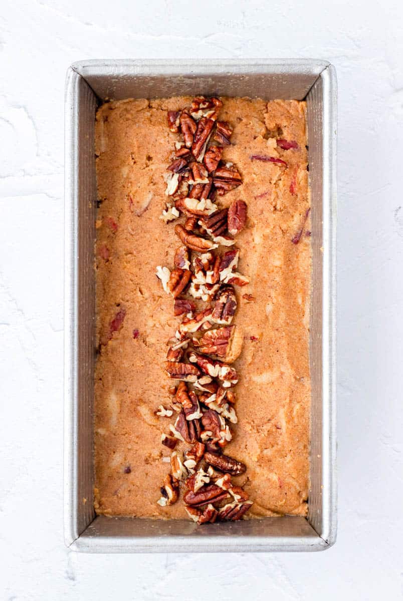 Pumpkin loaf batter in a loaf pan topped with pecans