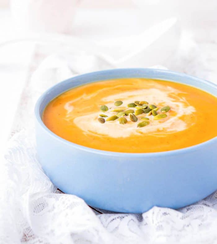 Butternut squash soup served in a blue bowl and topped with pumpkin seeds and coconut cream.