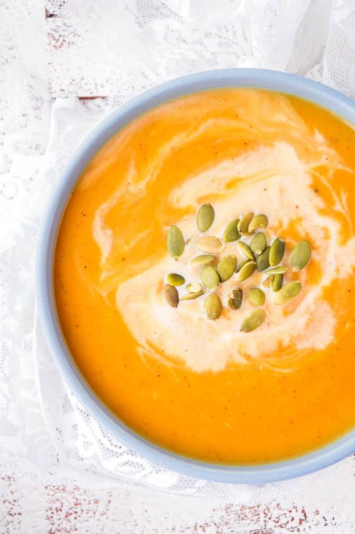 Top down shot of butternut squash soup in a blue bowl topped with pumpkin seeds.