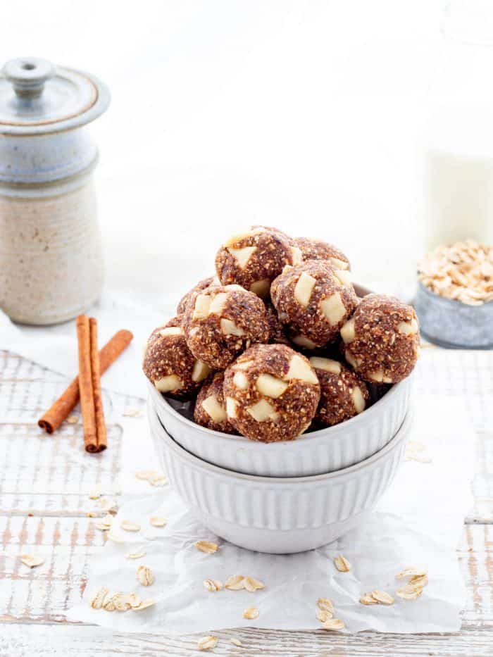 Bowl of energy balls with oats, cinnamon sticks and jug of milk on rustic white board