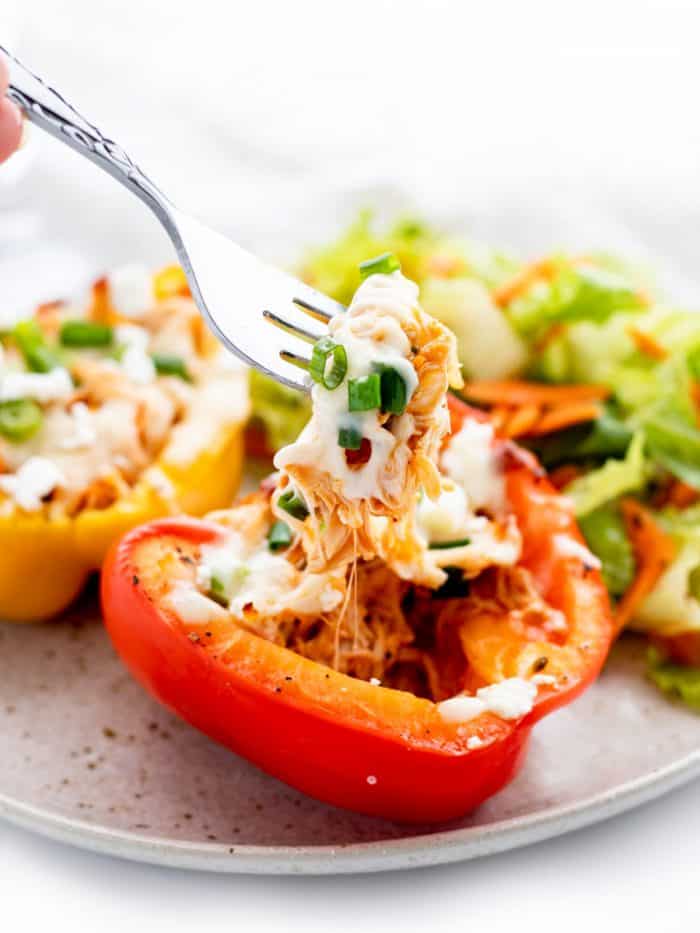 A fork picking up buffalo chicken and cheese out of a stuffed pepper with a side salad