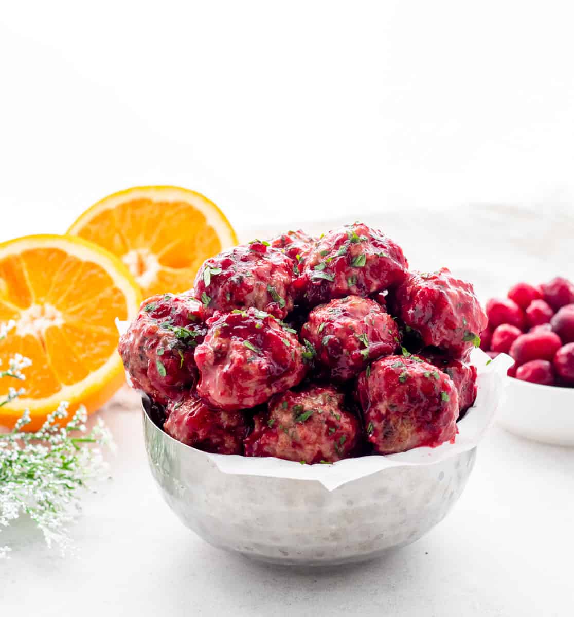 The cranberry meatballs in a bowl next to slices of orange.