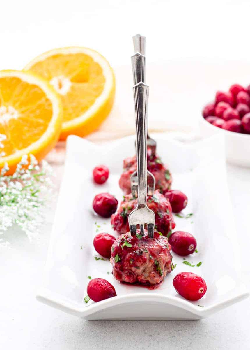 Cranberry meatballs on a white serving plate with small forks in them.