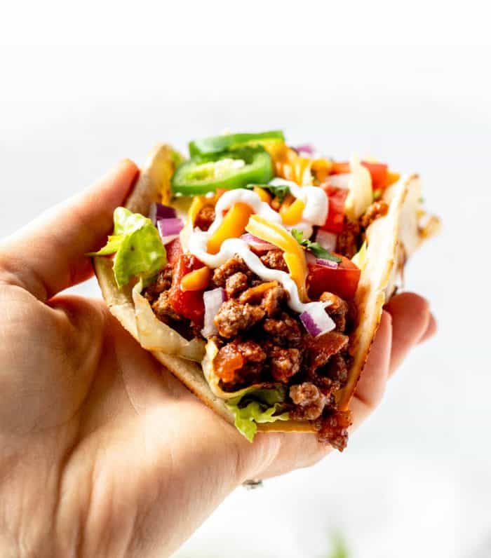 A hand holding a taco with Crock Pot taco meat and toppings.