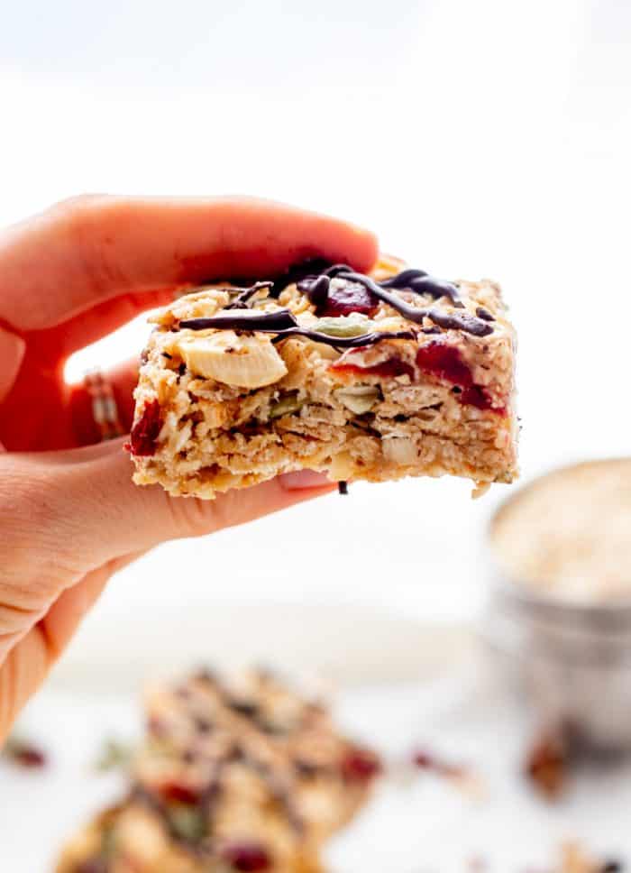 Holding a chewy homemade granola bar with chocolate drizzle.