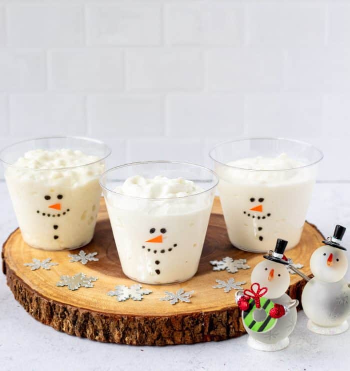 three frosty cups on a log slice next to snowmen