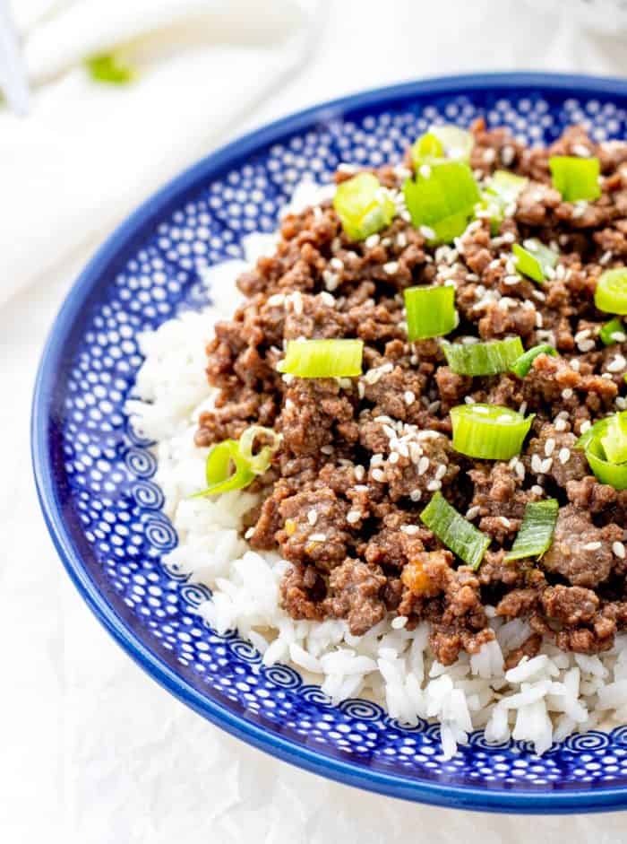 The cooked beef served on top of white rice and garnished with green onions and sesame seeds.