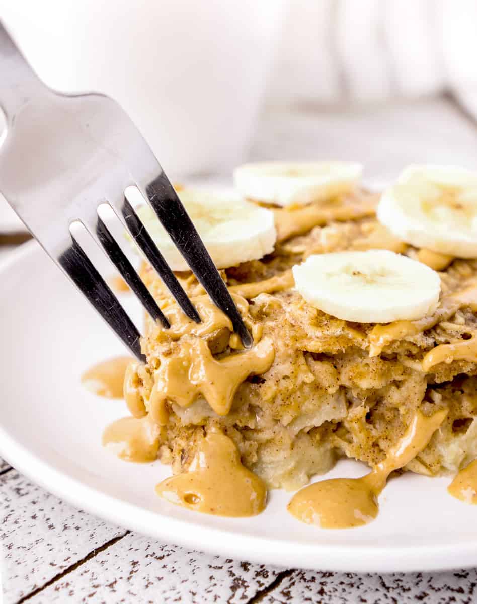 A fork digging into a slice of Baked Oatmeal with peanut butter drizzle