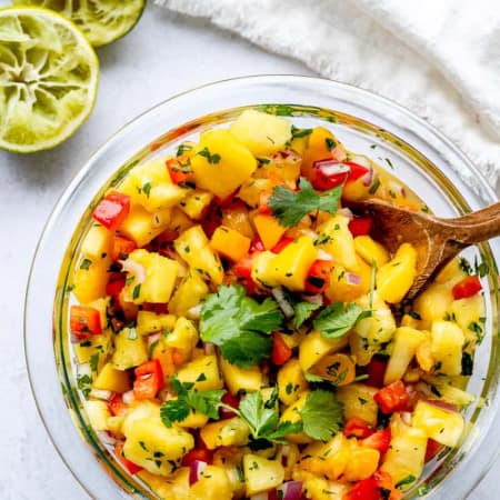 A bowl of pineapple mango salsa with a wooden spoon in it.