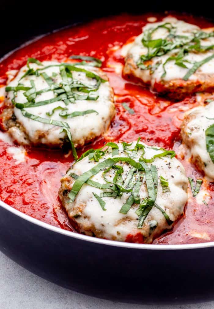 Close up of four chiken parmesan burgers in a skillet.