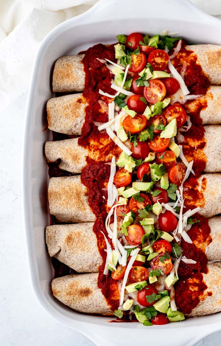 The baked enchiladas in a white dish topped with fresh toppings.