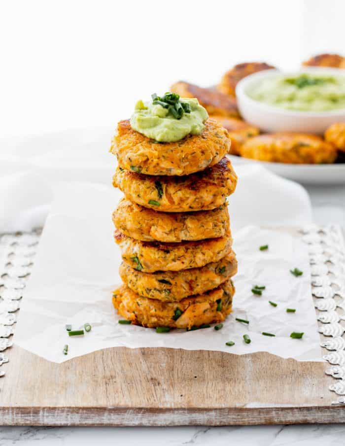 Six salmon cakes stacked on top of each other and topped with avocado crema.