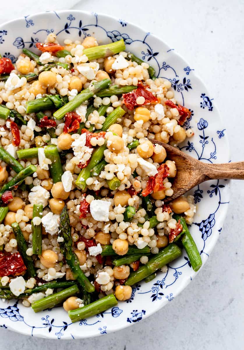 Pearl couscous salad in a blue and white bowl with a wooden spoon.