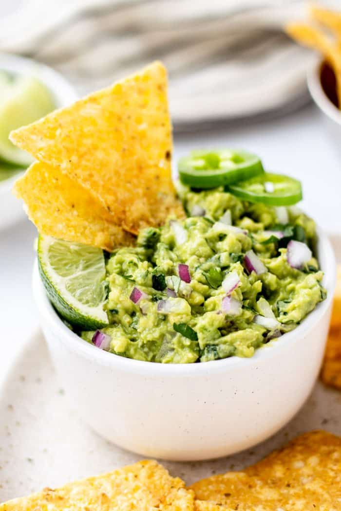 A bowl of guacamole topped with a lime wedge and jalapeno slices.