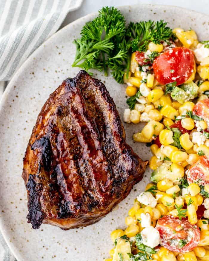 Marinaded steak served on a plate with a corn salad.